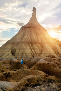 Back view of male tourist in summer wear standing on dried soil in bardenas reales and enjoying amazing view of natural rocky formation