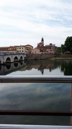 Arch bridge over river by buildings against sky in city