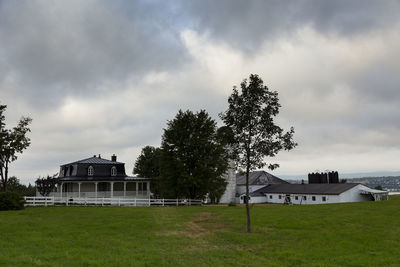 Building by trees on field against sky