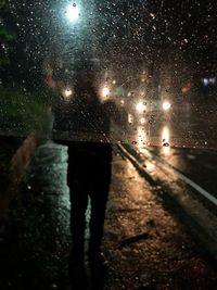 Rear view of person walking on wet street at night