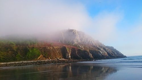 Rock formation by sea against sky during foggy weather