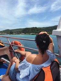 Rear view of woman sitting on boat in sea against sky