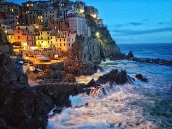 Illuminated houses by sea against sky at night