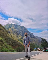 Full length of man wearing mask standing on road against mountain and sky