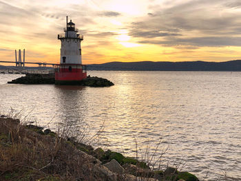 Lighthouse by sea against sky during sunset