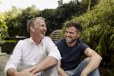 Father and son laughing while sitting together in backyard