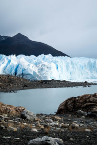 Lake and glacier against snowcapped mountains and cloudy sky