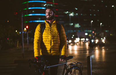 Man standing with bicycle on street in city at night