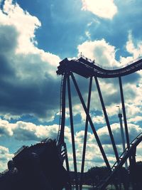 Silhouette of rollercoaster rides against cloudy sky