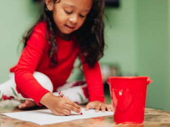 Mixed race girl at home in red shirt coloring in coloring book on coffee table 