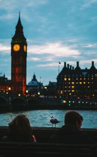 Rear view of people sitting at thames riverbank in city