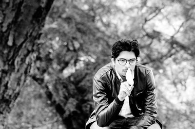 Thoughtful young man holding mobile phone while sitting at park