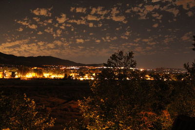 Illuminated trees on silhouette landscape against sky at night