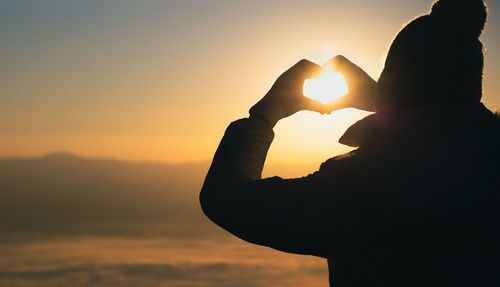 Silhouette woman holding heart shape against sky during sunset