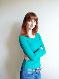 Portrait of smiling young woman with arms crossed standing against wall