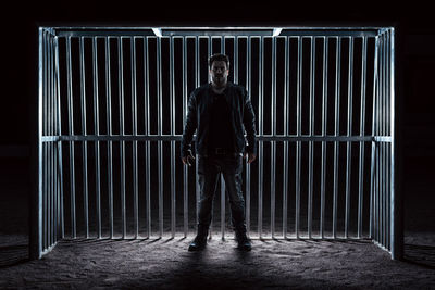 Portrait of man standing against metal grate in darkroom
