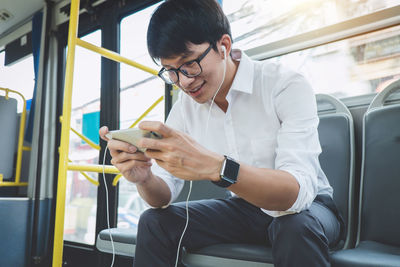 Smiling young man using mobile phone while sitting in bus