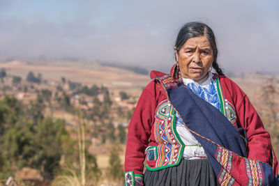 Senior peruvian female farmer in traditional costume standing in rural field in sunny day in chinchero