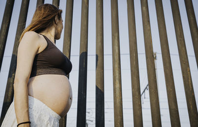 Side view of pregnant woman standing against gate