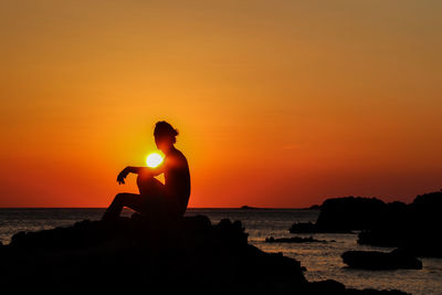 Silhouette woman sitting on rock against sky during sunset