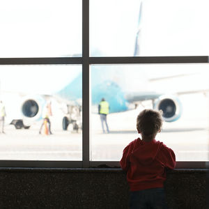 Rear view of boy looking through window at airport terminal