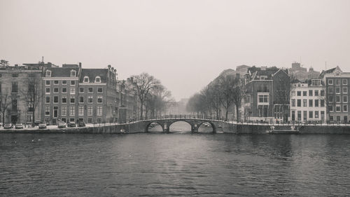 Bridge over river by buildings against sky in city