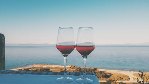 Wine glass on table by sea against clear sky