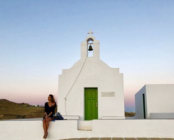 Woman sitting on bell tower against clear sky