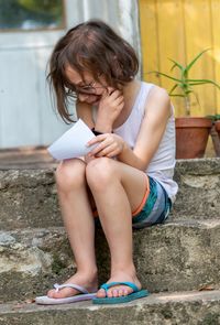 Full length of kid, holding a sheet of paper sitting outdoors