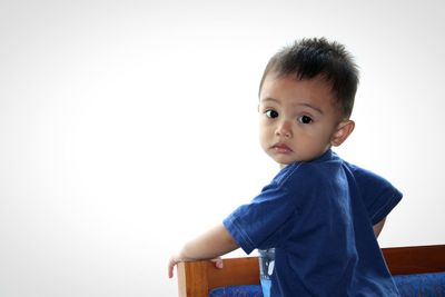 Portrait of cute boy standing on sofa against white background