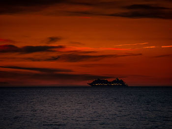 Illuminated cruise ship on the sea in front of red sky just after sunset