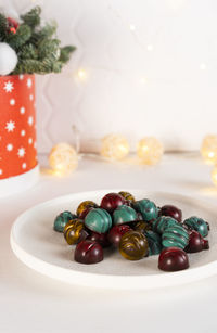 Green, yellow and red homemade chocolate candies in the shape of christmas balls on a white plate.