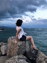 Full length of woman on rock at sea shore against sky