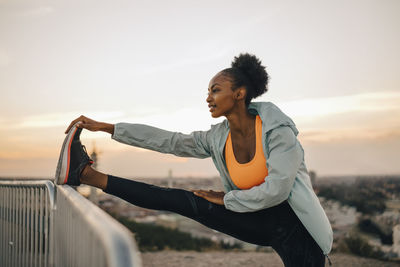 Sportswoman doing stretching exercise against sky during sunset