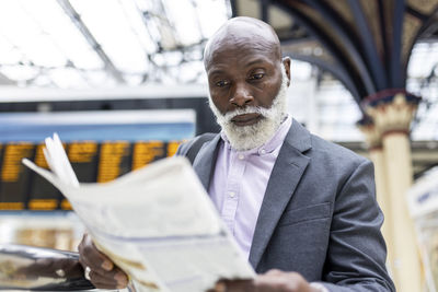 Senior businessman reading newspaper at railroad station