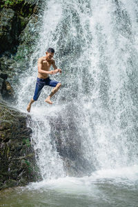 Full length of shirtless man jumping on waterfall