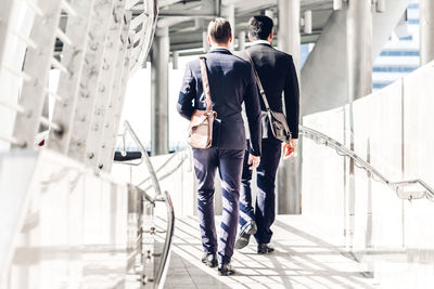 Rear view of businessmen walking on footbridge in city