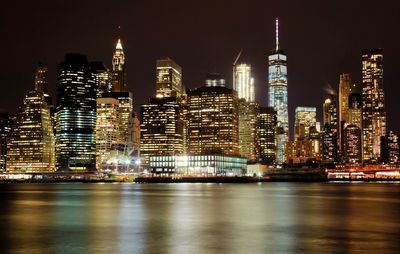 Illuminated cityscape by sea against sky at night