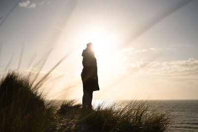 Woman standing by sea against sky during sunset