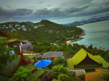 High angle view of houses and trees by lake against sky