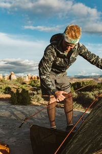 Male hiker in headband and camo jacket sets up camp in desert