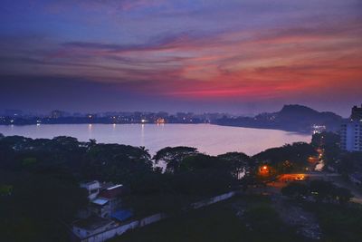 Illuminated city by sea against sky during sunset