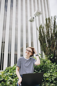 Smiling woman with hand in hair in front of building