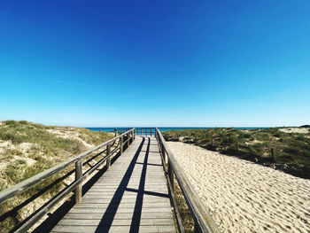 View of wooden footbridge against clear blue sky