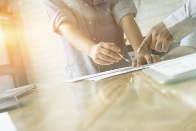 Midsection of colleagues analyzing charts on office desk