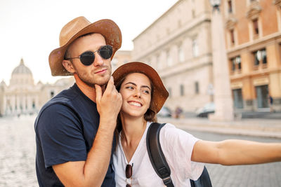 Portrait of smiling young woman wearing hat standing in city