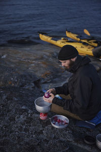 Man preparing food at sea, kayaks in background