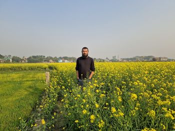 Rear view of man standing amidst yellow flowering plants on field against sky