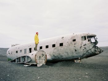 Man standing on airplane wreck against sky