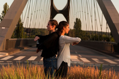 Female friends dancing against bridge in city during sunset